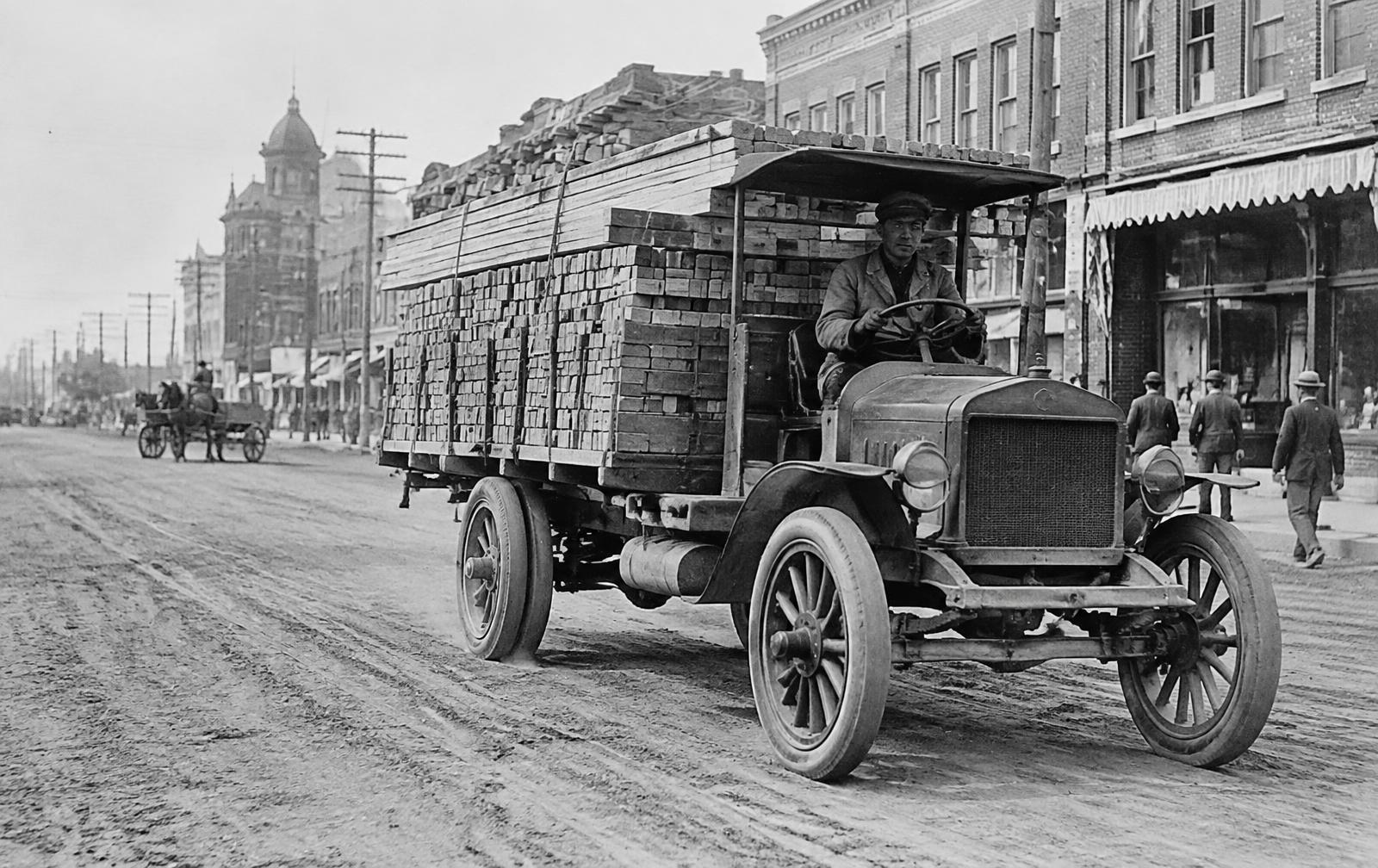 Archival-style photograph of an early motor truck carrying brick and lumber through a Texas city